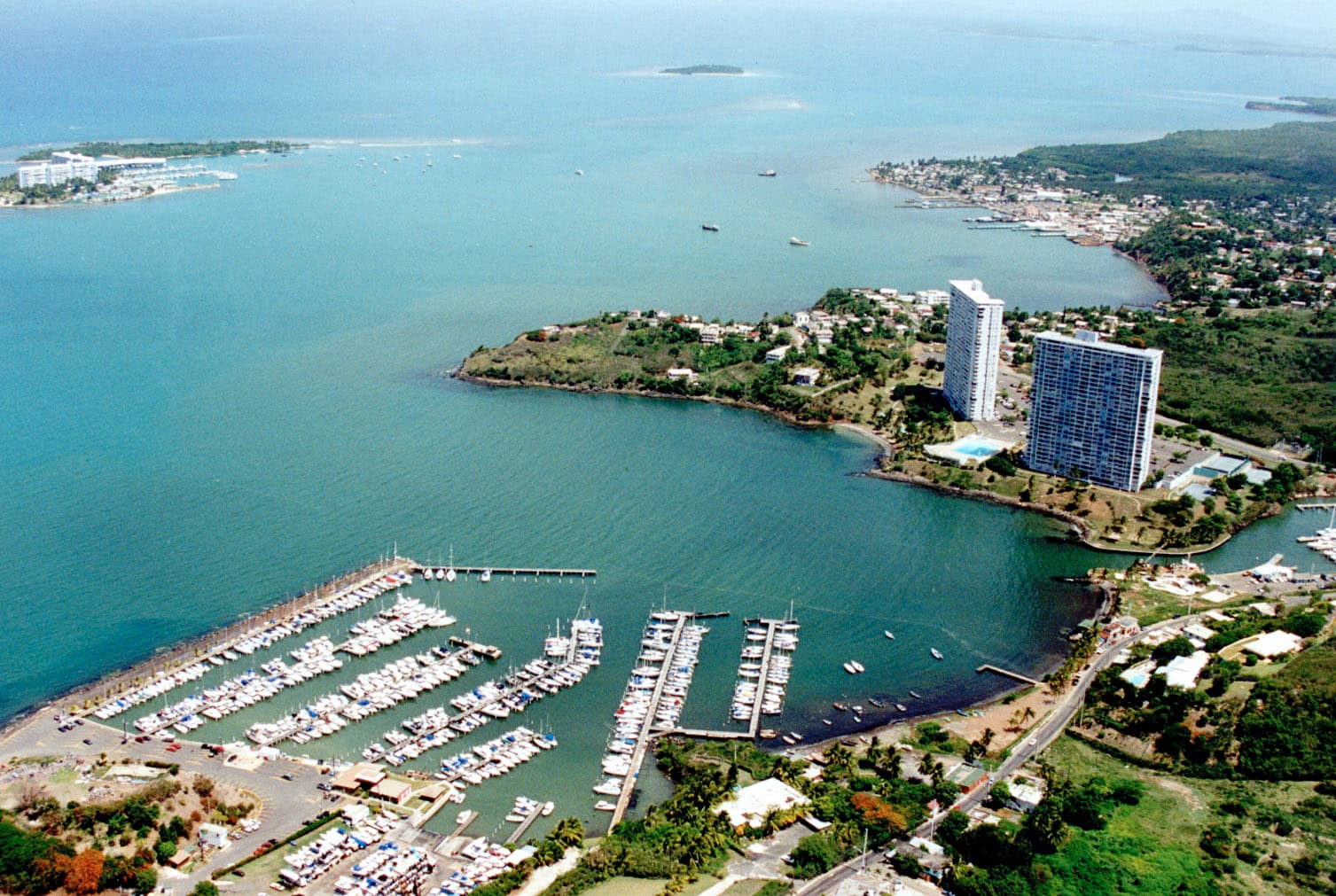Vista aérea de una marina con botes atracados, torres de condominios costeros y el litoral de Fajardo.