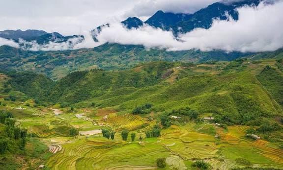 Terraced green hills below a cloud-covered mountain ridge.