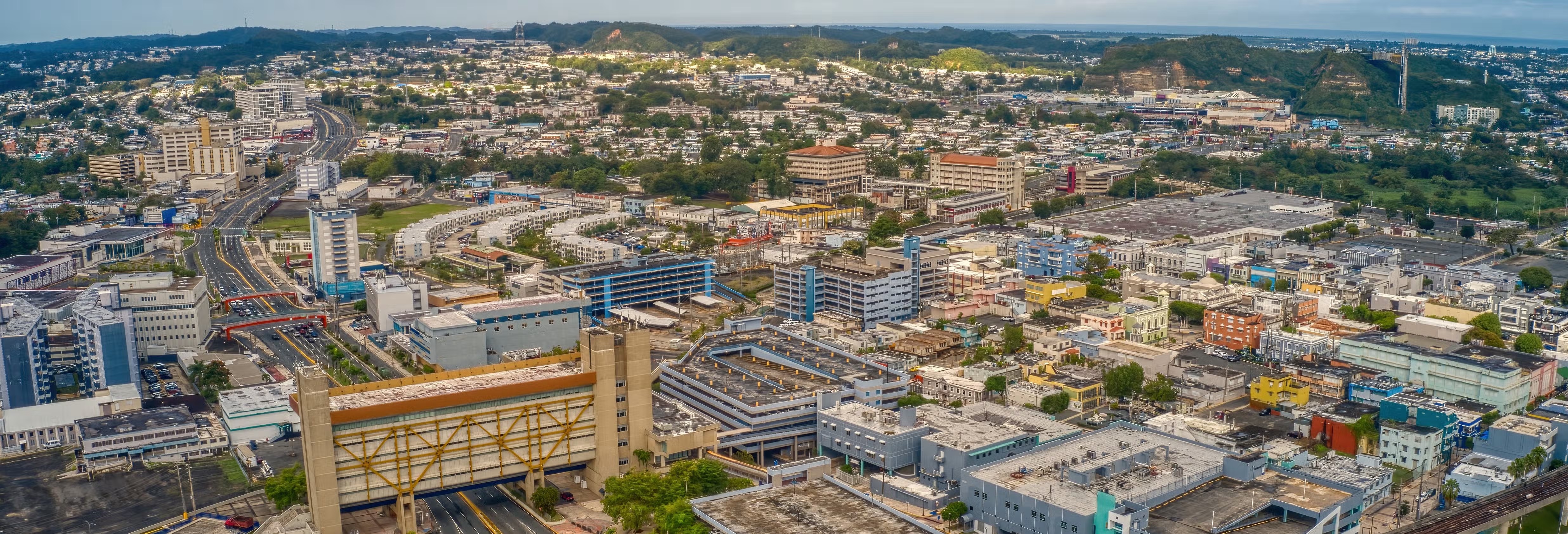 Wide aerial view of Bayamon's urban core, highway corridors, and surrounding hills.